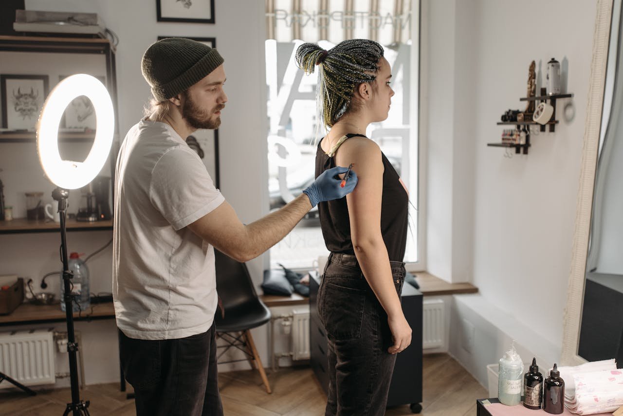 services-02 Tattoo artist precisely working on a woman's shoulder in a modern studio environment.